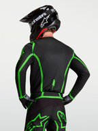 Alpinestars Fluid Apex V2 jersey, motocrossjersey voor heren, zwart en fluoriserend groen, vochtafvoerend textiel met verlengde achterkant, getoond op een rijder met bijpassende helm.