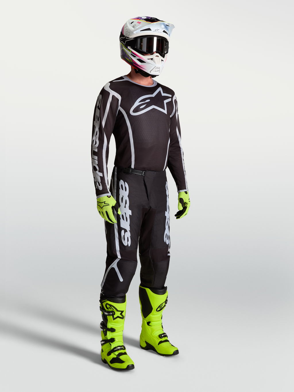 Alpinestars Fluid Apex V2 jersey, zwart en zilver, motorcrossuitrusting met neon groene motorlaarzen en motorhandschoenen.