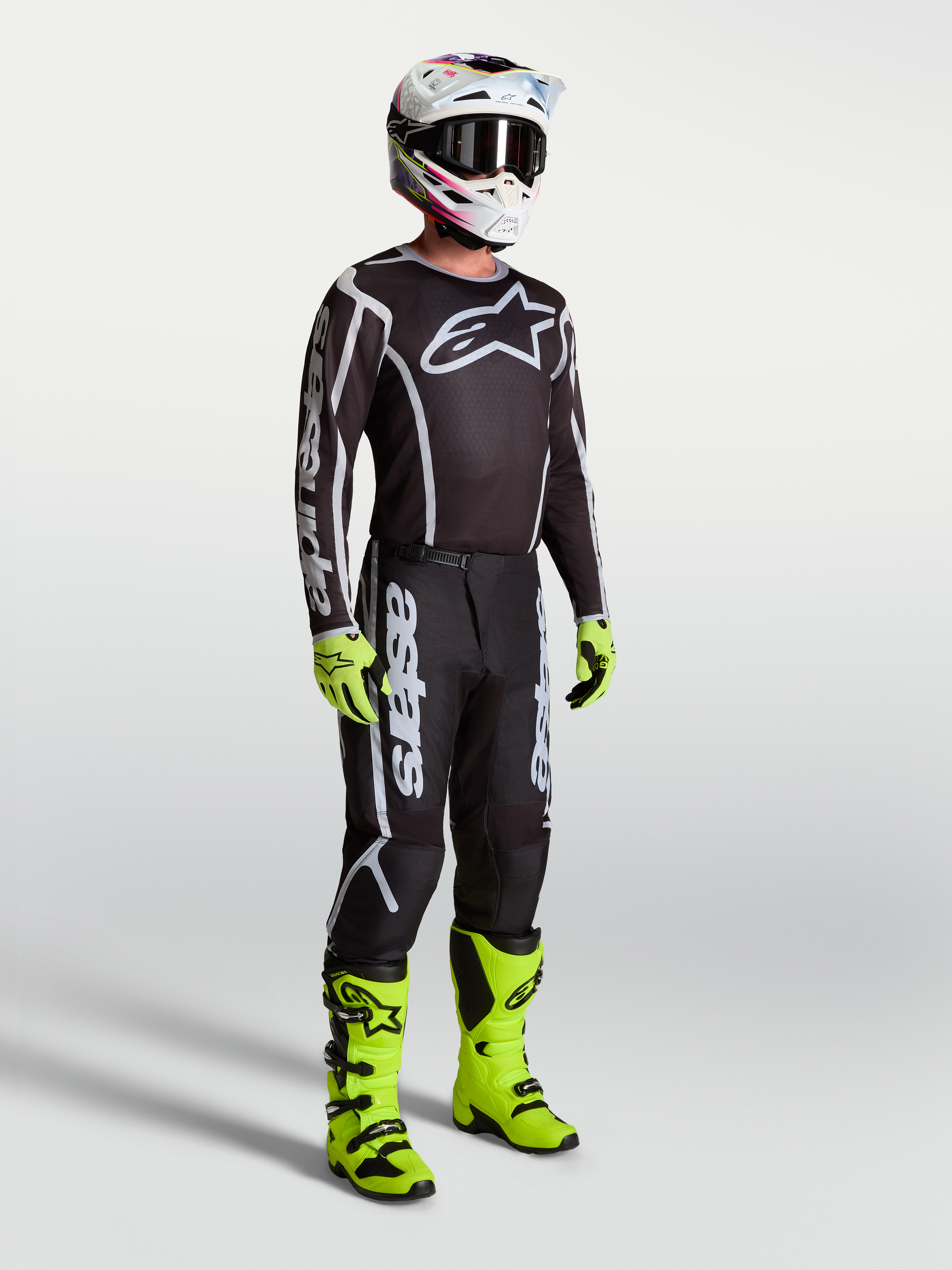 Alpinestars Fluid Apex V2 jersey, zwart en zilver, motorcrossuitrusting met neon groene motorlaarzen en motorhandschoenen.