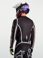 Alpinestars Fluid Apex V2 Jersey, zwart en zilver motocross shirt op model van achteren gezien, vochtafvoerend polyfabric en ergonomische snit.