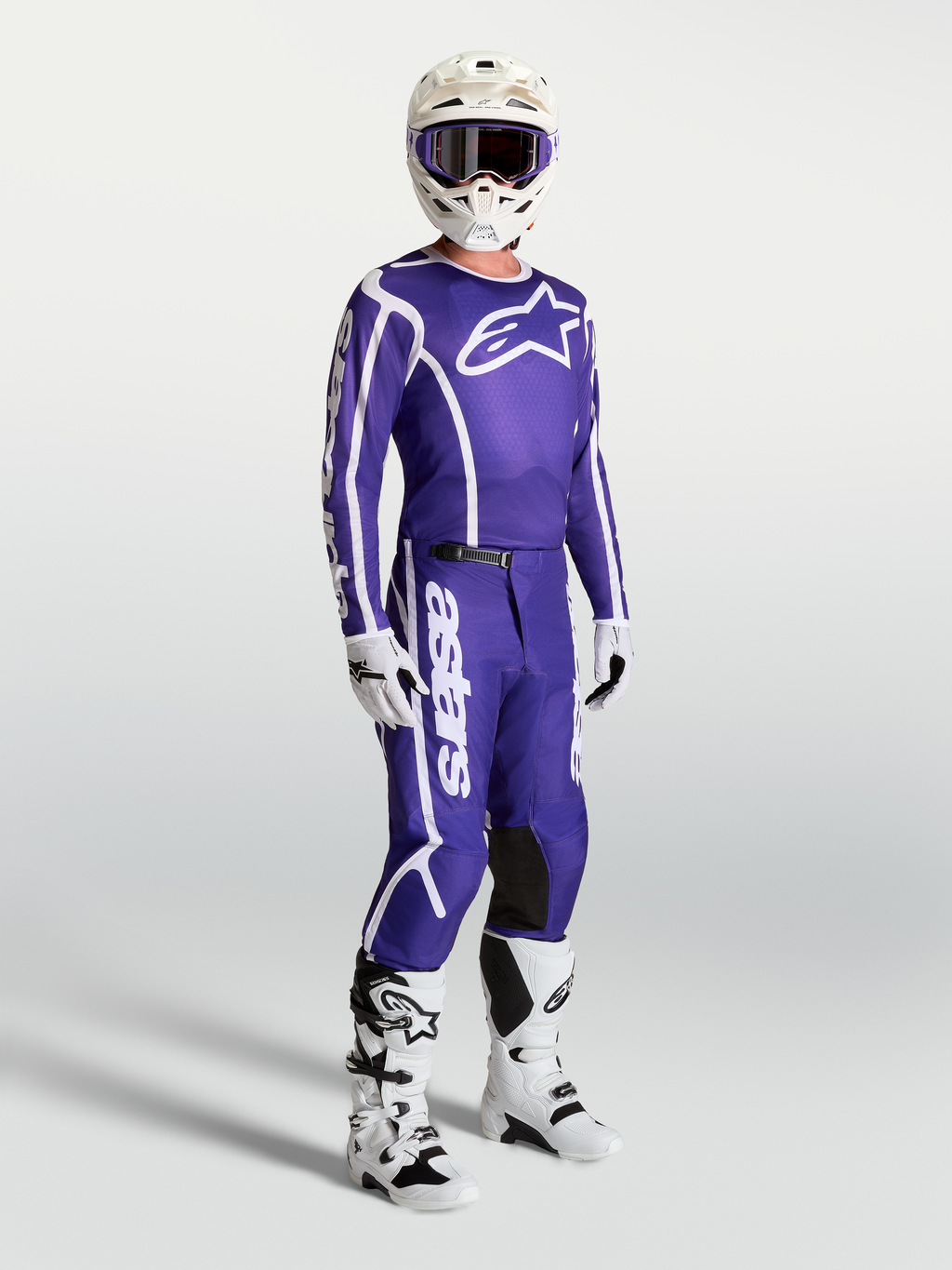 Alpinestars Fluid Apex V2 jersey en broek, blauwe en witte motocross-set op model met witte motorlaarzen en helm.