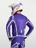 Alpinestars Fluid Apex V2 jersey, heren motorcrossjersey, blauw en wit, ademende polyfabric constructie, getoond vanaf de rugzijde op een model met helm.