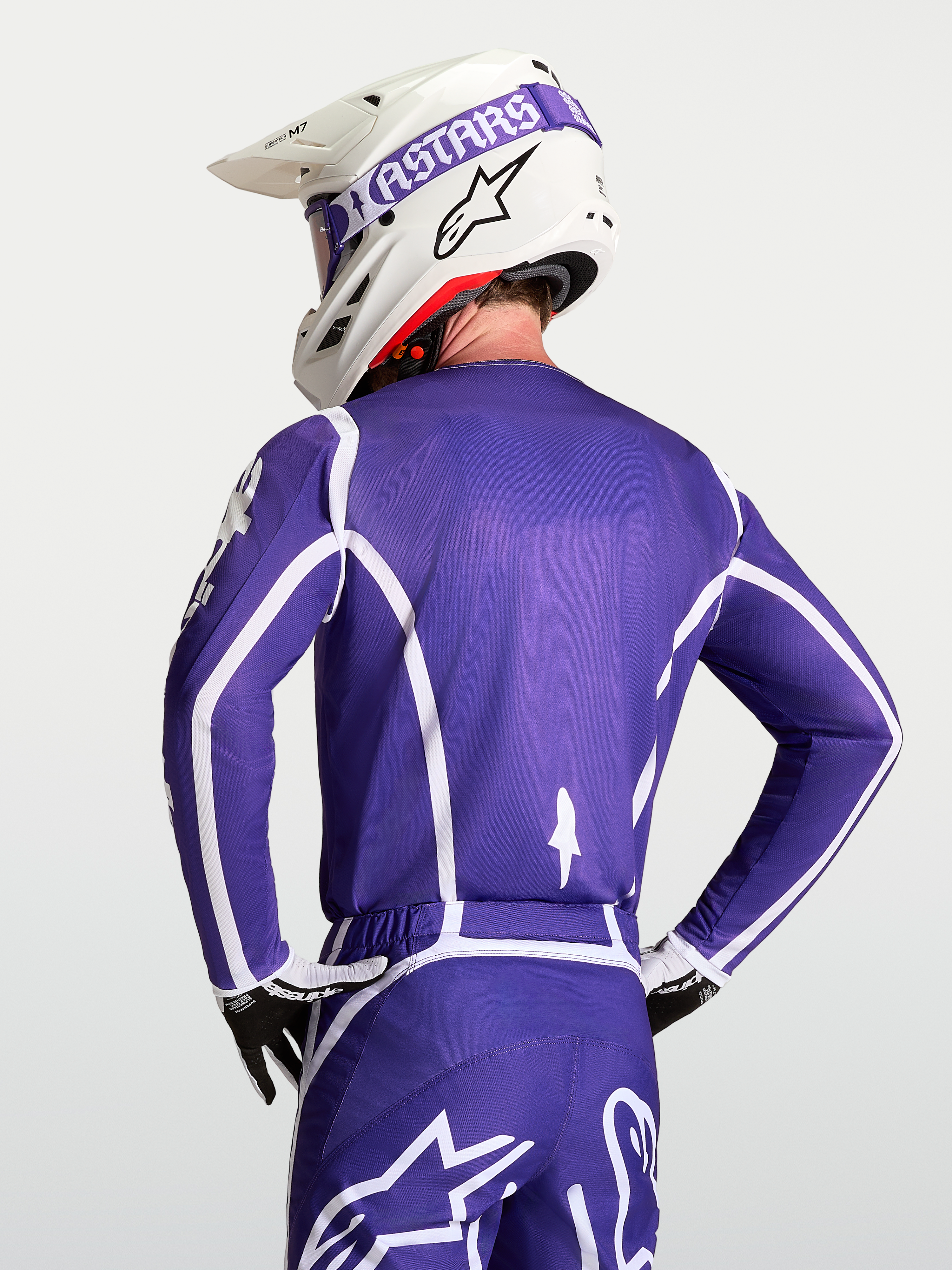 Alpinestars Fluid Apex V2 jersey, heren motorcrossjersey, blauw en wit, ademende polyfabric constructie, getoond vanaf de rugzijde op een model met helm.