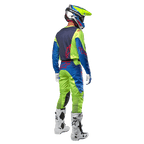 Motocrossrijder van achteren gezien die de Alpinestars 2024 Racer Hoen Jersey draagt in Yellow Fluo en Blue Night Navy, bijpassende motorcrossbroek en witte laarzen, toont het ontwerp aan de achterzijde met rode logo's, gecoördineerde outfit voor professioneel off-road racen