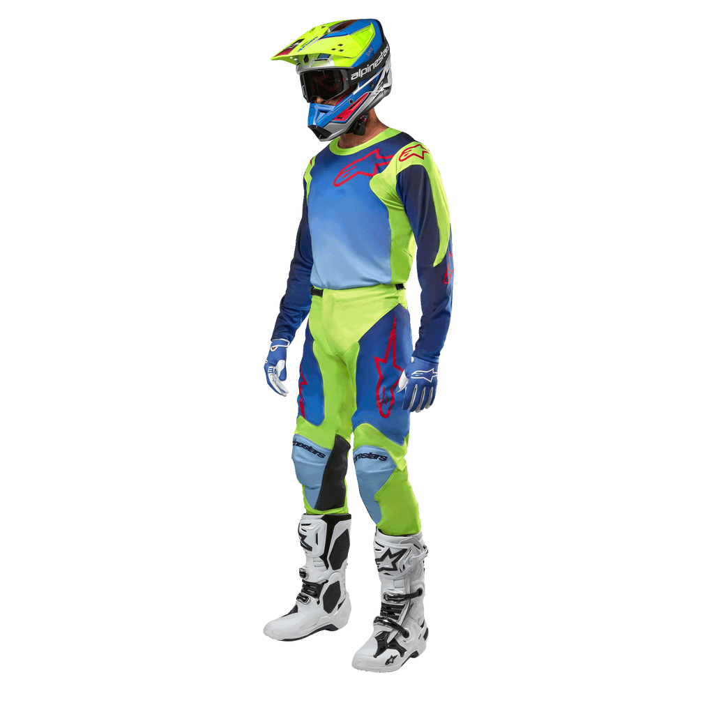 Alpinestars 2024 Racer Hoen Jersey, motocross shirt, geel fluo en blauw night navy, gedragen door een rijder met bijpassende broek, helm en witte laarzen, professionele race-uitrusting voor off-road rijden