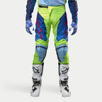 Alpinestars 2024 Racer Hoen broek, motorcrossbroek, fluoriserend geel en nachtblauw, gedragen met witte en zwarte motorcrosslaarzen en blauwe handschoenen, voorzien van opvallende rode logo's, lichtblauwe kniepanelen en een sportief ergonomisch ontwerp voor off-road rijden