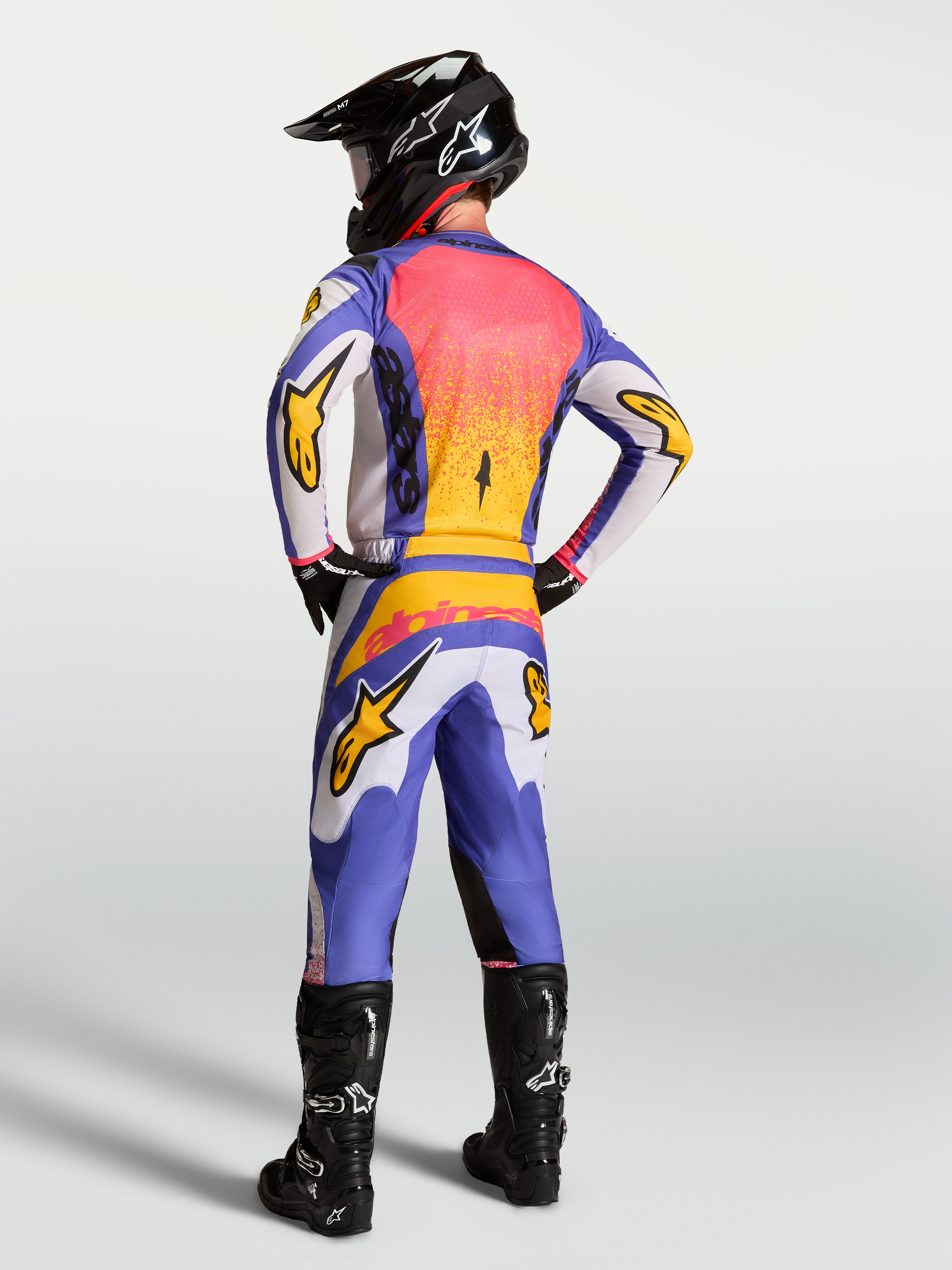 Alpinestars Fluid Drag jersey, lila en blauw met goud, motorcrosser van achteren in volledige MX-uitrusting.