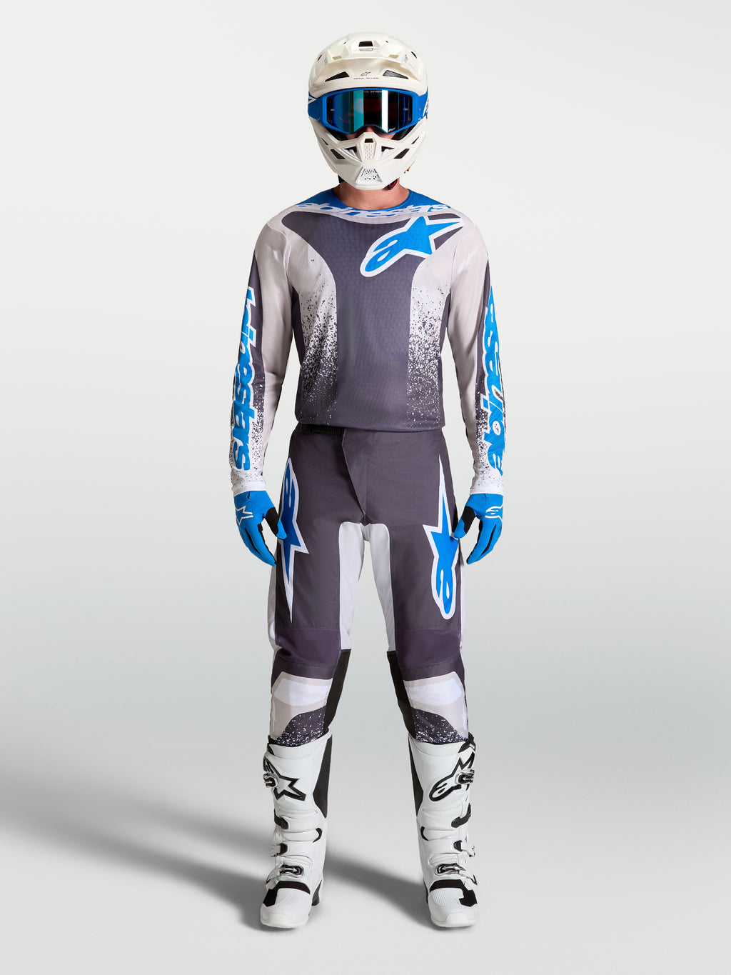 Alpinestars Fluid Drag Jersey in grijs en blauw, gedragen als motocross-uitrusting met witte helm en motorlaarzen.