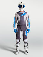 Alpinestars Fluid Drag Jersey in grijs en blauw, gedragen als motocross-uitrusting met witte helm en motorlaarzen.