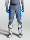 Alpinestars Racer Amber broek 2027, heren-motocrossbroek in grijs en blauw, gedragen met witte motorlaarzen.
