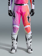 Alpinestars 2026 Racer Air Portl broek, motorcrossbroek, levendig kleurverloop van paars, roze en oranje, met opvallende sterlogo's op de dijen, gedragen met witte racelaarzen en zwarte handschoenen, ontworpen voor high-performance off-road rijden