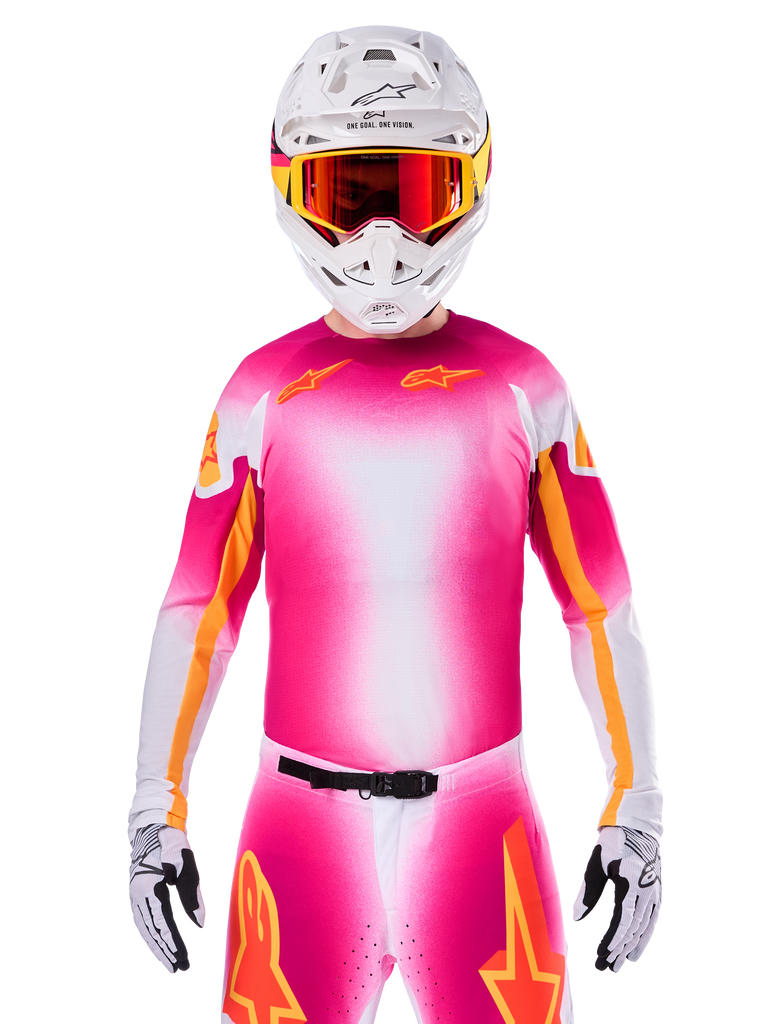 Motocross rider wearing the Alpinestars Limited Edition Supertech AFD MIG Jersey, Pink Fluo White gradient design with orange star logos, matching pants, white helmet, and red-tinted goggles, elite off-road racing apparel.