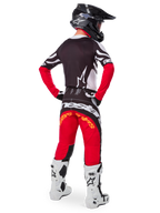 Rear view of a motocross rider wearing the Limited Edition Techstar Deep Gear Set, featuring a black jersey with white and red accents, matching red and black pants with 'Alpinestars' branding, white racing boots, and a black helmet, showcasing the complete off-road racing outfit.