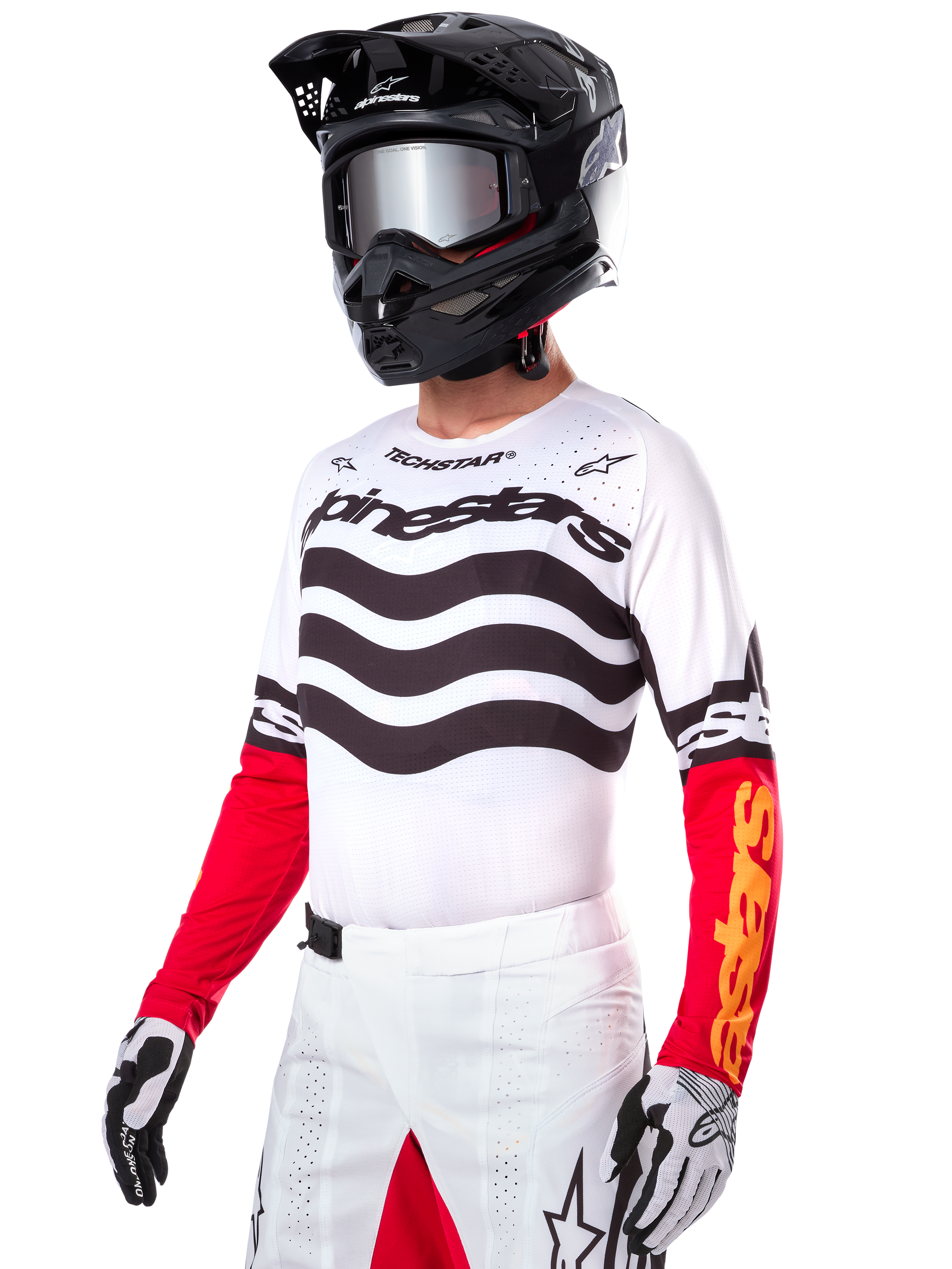 Alpinestars Limited Edition Techstar Deep Jersey, motorcrosser met een wit shirt met zwarte golvende strepen en rode onderkant van de mouwen, gecombineerd met een zwarte helm, spiegelende crossbril, wit-zwarte handschoenen en witte crossbroek, performance motorcross outfit.