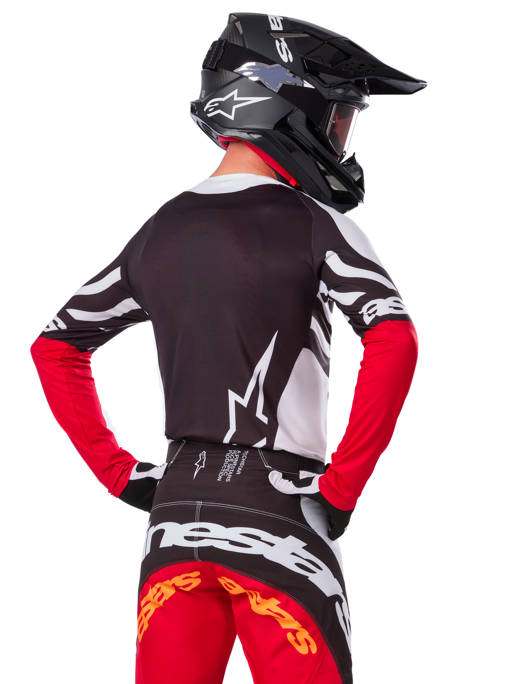 Motocrossrijder vanaf de achterkant in de Alpinestars Limited Edition Techstar Deep Jersey, zwart, wit en High Red, met bijpassende crossbroek en een zwarte helm, atletische pasvorm voor off-road prestaties