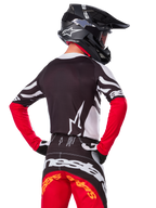 Motocrossrijder vanaf de achterkant in de Alpinestars Limited Edition Techstar Deep Jersey, zwart, wit en High Red, met bijpassende crossbroek en een zwarte helm, atletische pasvorm voor off-road prestaties