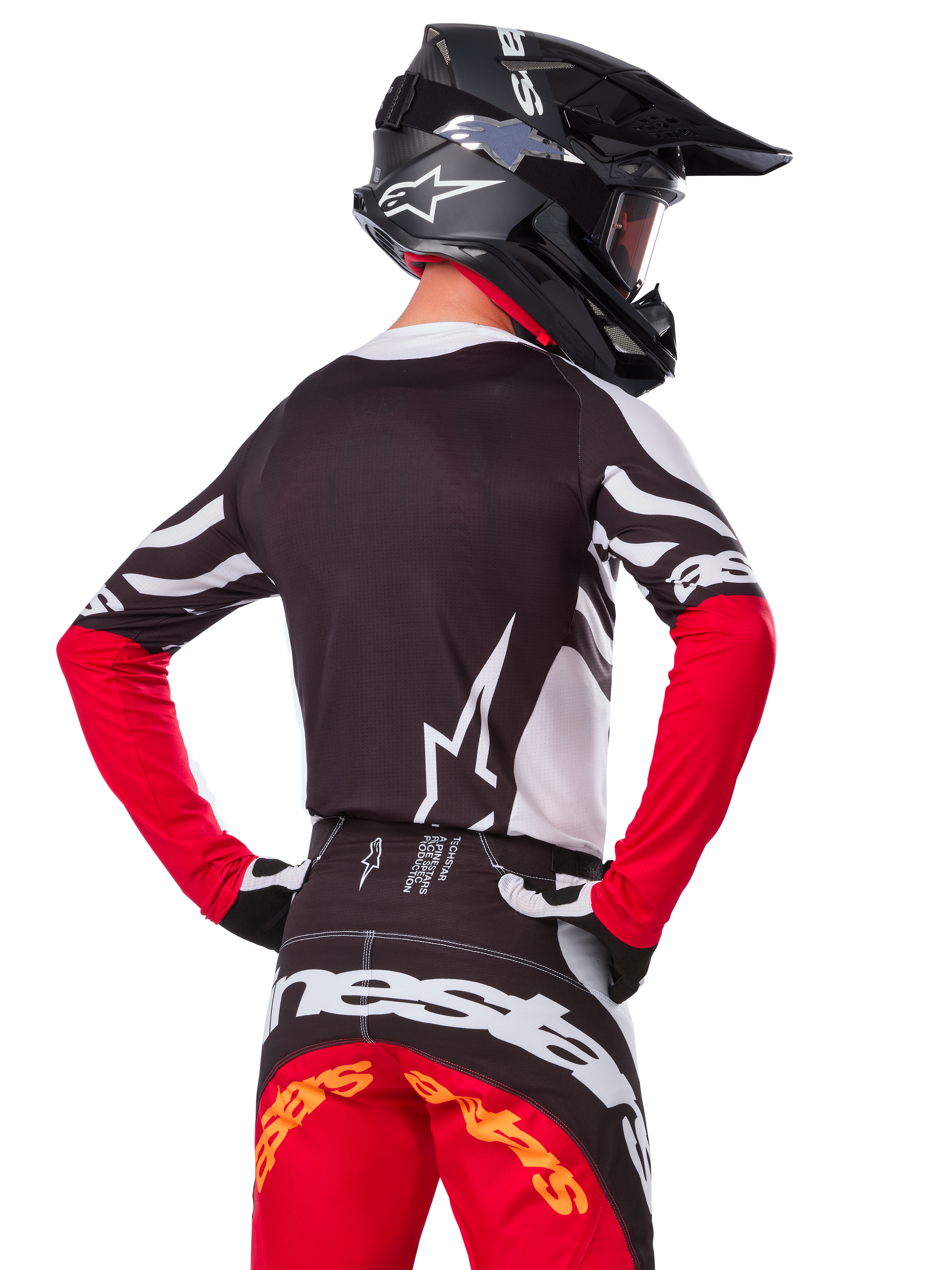 Motocrossrijder vanaf de achterkant in de Alpinestars Limited Edition Techstar Deep Jersey, zwart, wit en High Red, met bijpassende crossbroek en een zwarte helm, atletische pasvorm voor off-road prestaties