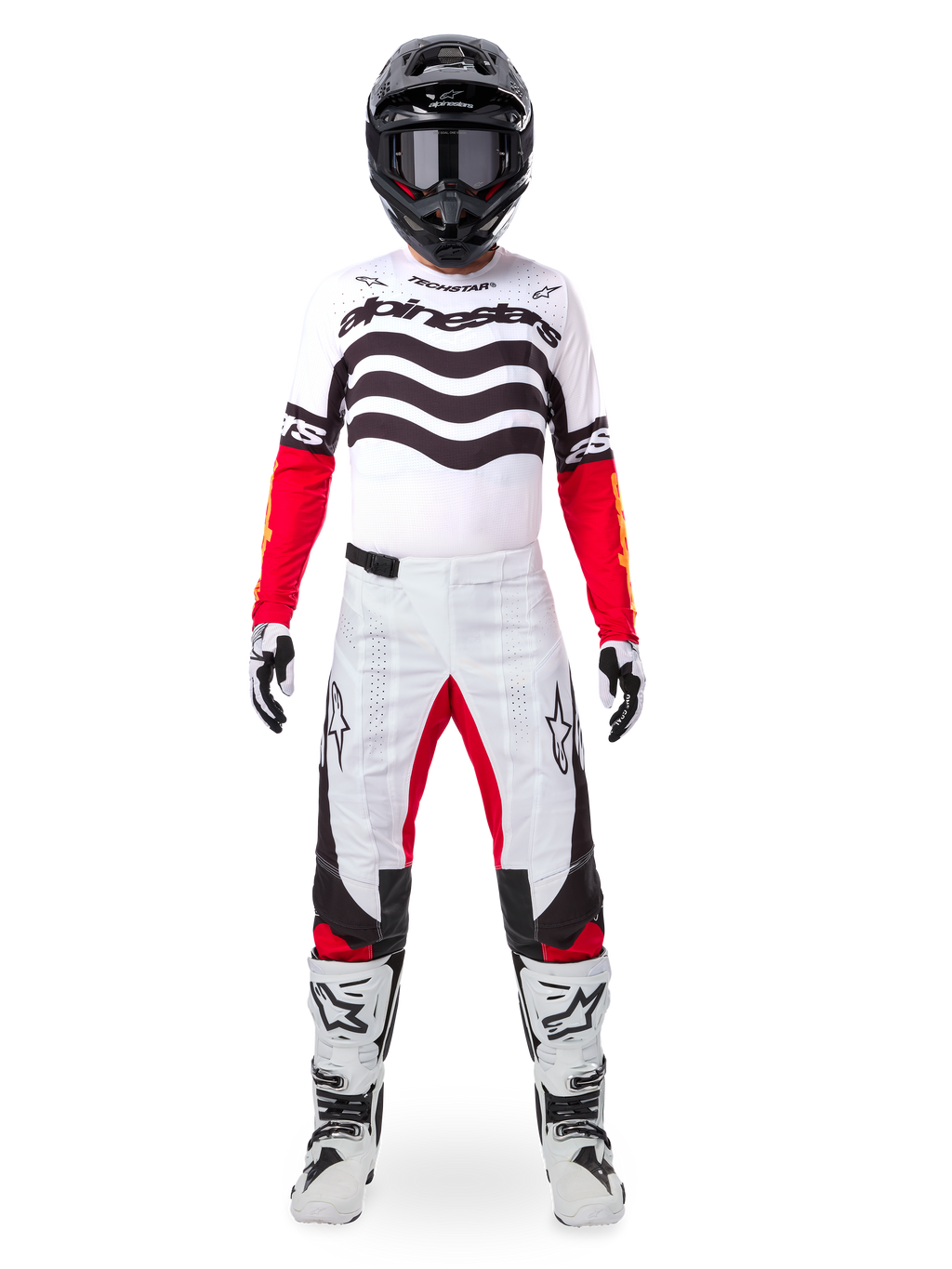 Motocrosser die de Alpinestars Limited Edition Techstar Deep Jersey draagt in wit, zwart en rood, met golvende graphics op de borst, gecombineerd met een bijpassende wit-rode broek, een zwarte helm en witte racelaarzen, volledige professionele off-road uitrusting.