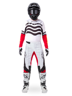 Motocrosser die de Alpinestars Limited Edition Techstar Deep Jersey draagt in wit, zwart en rood, met golvende graphics op de borst, gecombineerd met een bijpassende wit-rode broek, een zwarte helm en witte racelaarzen, volledige professionele off-road uitrusting.
