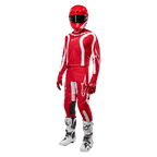 Motorcrosser in volledige race-uitrusting, Alpinestars 2024 Fluid Lurv Jersey in Mars Red en wit, bijpassende rode broek met witte accenten, rode helm, rode handschoenen en witte en zwarte laarzen, gecoördineerde outfit voor off-road racen