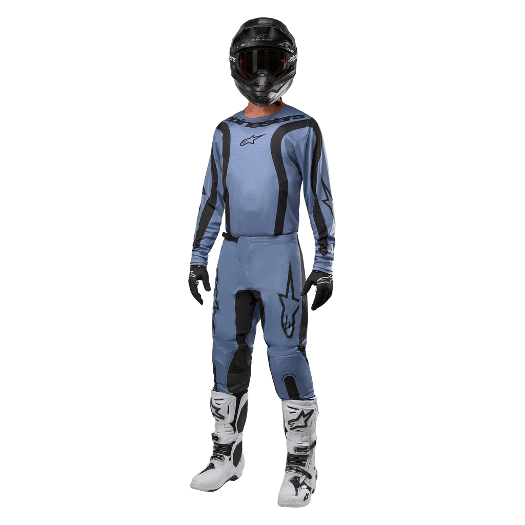 Motorcrossrijder in volledige race-uitrusting, Alpinestars 2024 Fluid Lurv Jersey in lichtblauw en zwart, bijpassende lichtblauwe broek met zwarte panelen, witte en zwarte laarzen, zwarte handschoenen en een zwarte helm met crossbril, gecoördineerde outfit voor off-road racing