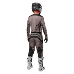 Alpinestars 2024 Fluid Lurv Jersey, motocross jersey, Mud Black, achteraanzicht van een motorcrossrijder in bijpassende race-uitrusting, zwarte helm en witte laarzen, met opvallende zwarte Alpinestars-logo's en een sportieve pasvorm voor off-road prestaties.