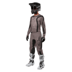 Motorcrossrijder in volledige race-uitrusting met de Alpinestars 2024 Fluid Lurv Jersey in Mud Black, gecombineerd met bijpassende broek, zwarte helm met goggle, wit-zwarte laarzen en zwarte handschoenen, gecoördineerde outfit voor off-road racen