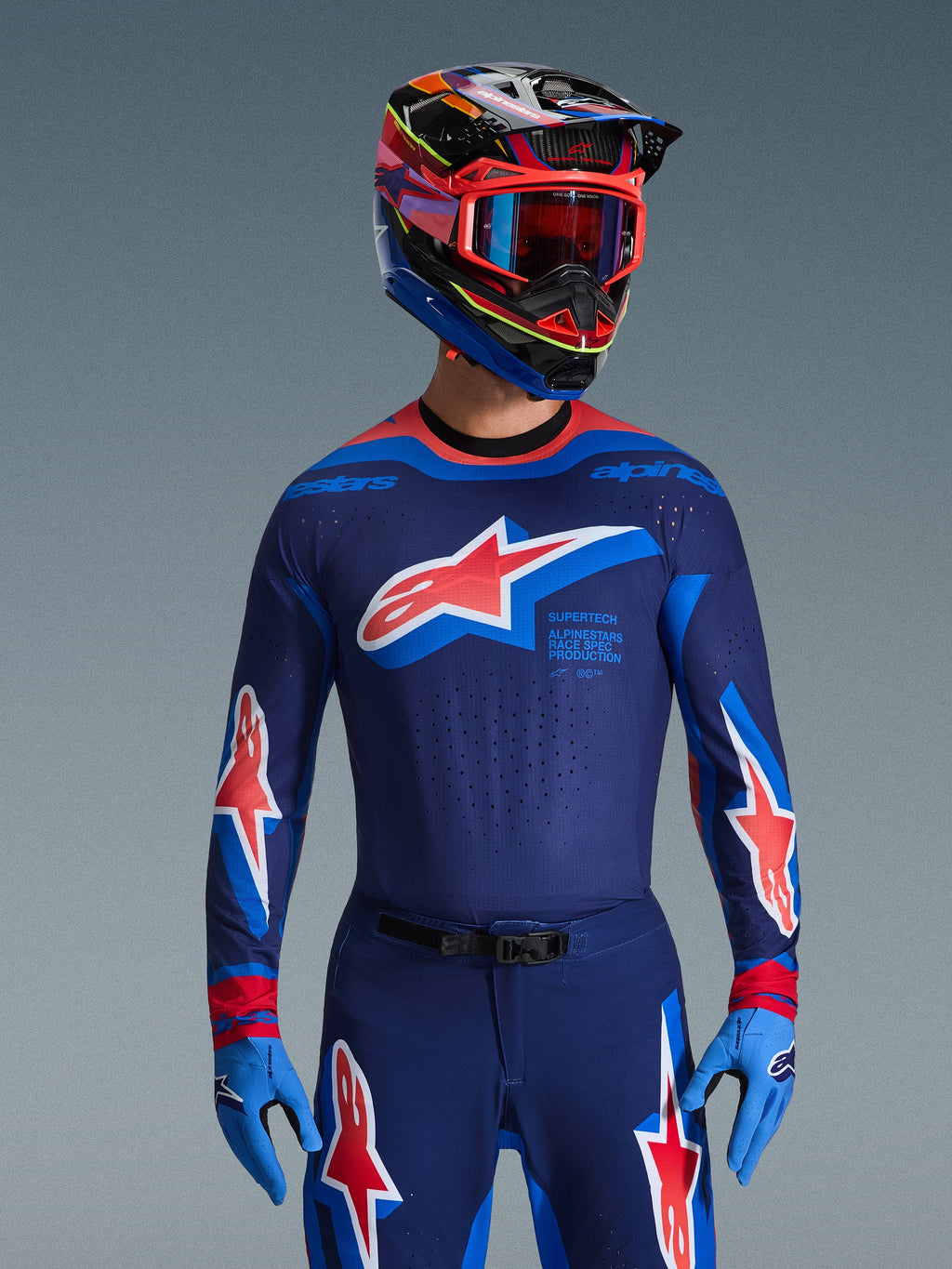 Alpinestars 2026 Supertech Vista Gear Set, professional motocross apparel, navy blue jersey and pants with bold red and white star logos, paired with a multi-colored racing helmet, red goggles, and light blue gloves, coordinated pro-level racing outfit
