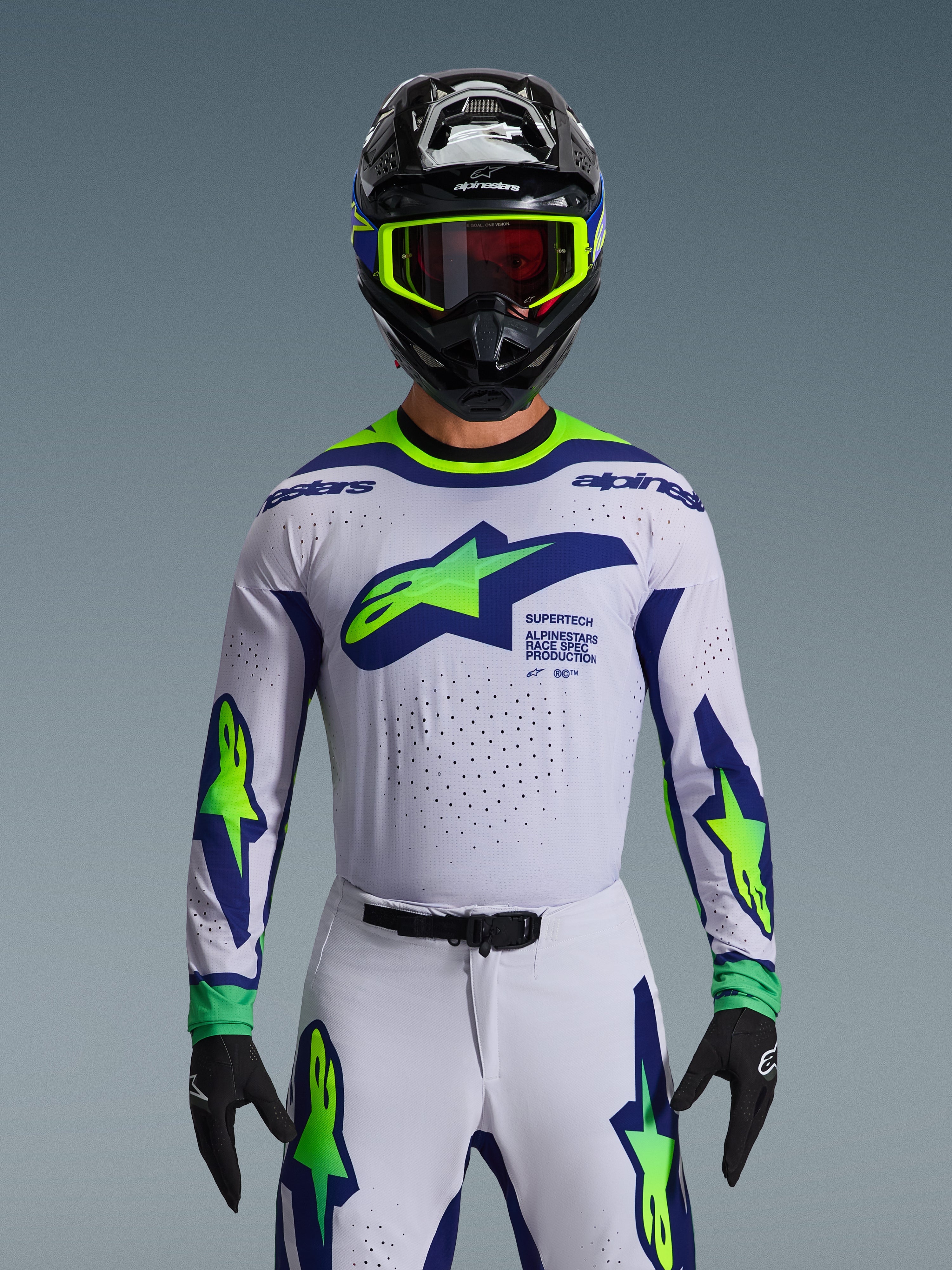 Alpinestars 2026 Supertech Vista Gear Set, Motocross Jersey and Pants, White with Blue and Neon Green graphics, worn with a black helmet and neon goggles, featuring laser-cut ventilation and athletic race fit for professional racing.