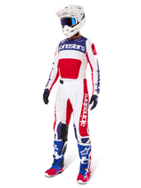 Motocross rider wearing complete racing gear, featuring the Alpinestars Limited Edition Techstar Fortitude Jersey in Bright Red, White, and Blue. Matching motocross pants, white helmet with blue goggles, and blue and red boots, providing a coordinated look for off-road competition.