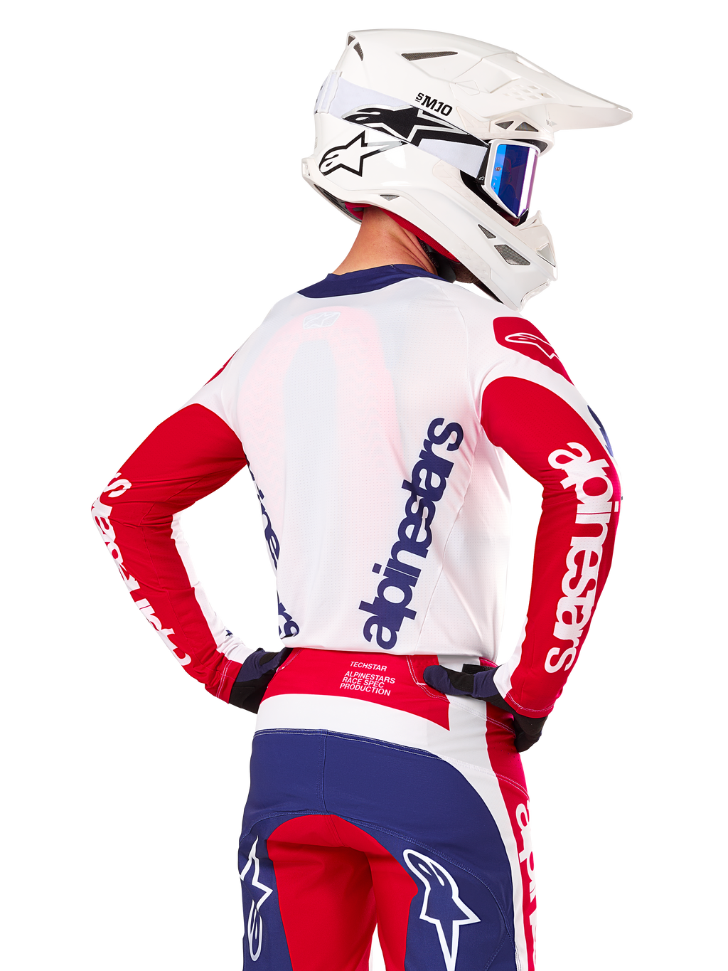 Alpinestars Limited Edition Techstar Fortitude Jersey, motocross shirt, felrood, wit en blauw, achteraanzicht van een rijder met een witte helm en bijpassende uitrusting, met opvallende Alpinestars-logo's op de rug en mouwen, ontworpen voor hoogwaardige off-road races.