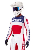 Motorcrosser die de Alpinestars Limited Edition Techstar Fortitude Jersey draagt, in felrood, wit en blauw, met een witte helm, blauwe crossbril en bijpassende broek, hoogwaardige racekleding voor off-road competitie