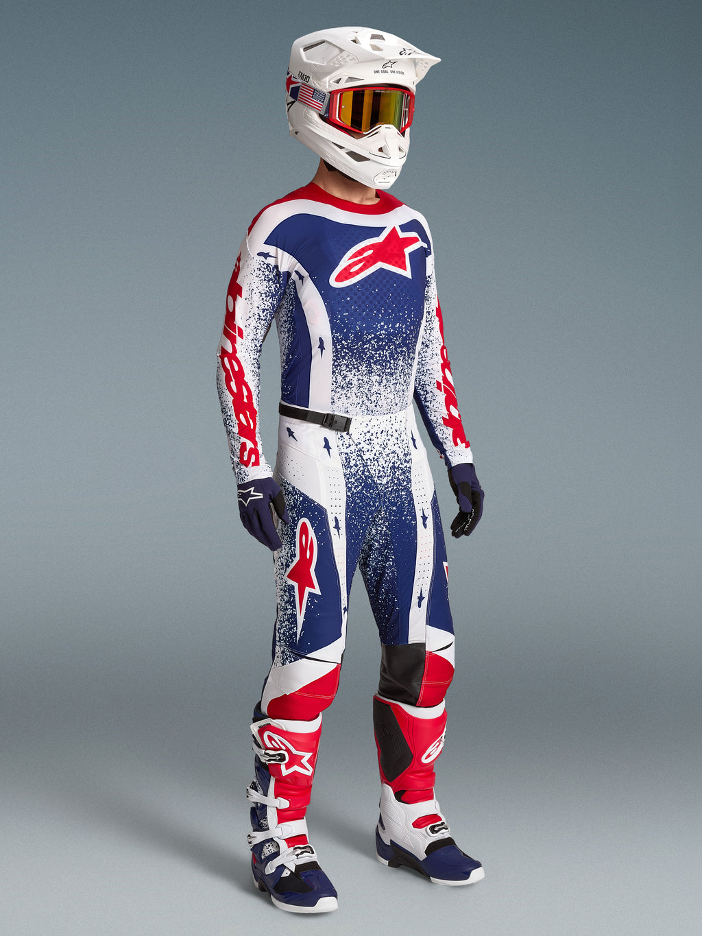 Alpinestars Techstar Unity beperkte oplage kledingset, rood, wit en blauwe motorcrossjersey en broek op model, inclusief bijpassende helm en motorlaarzen.