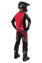 Motocrossrijder van achteren gezien in de 2024 Supertech Ward Jersey in Black Red Berry, voorzien van een felrood rugpaneel en zwarte mouwen met witte Alpinestars-branding. Gecombineerd met een bijpassende motorcrossbroek, zwarte Tech 10-laarzen en een zwarte helm van koolstofvezel voor een gecoördineerde professionele race-uitrusting.