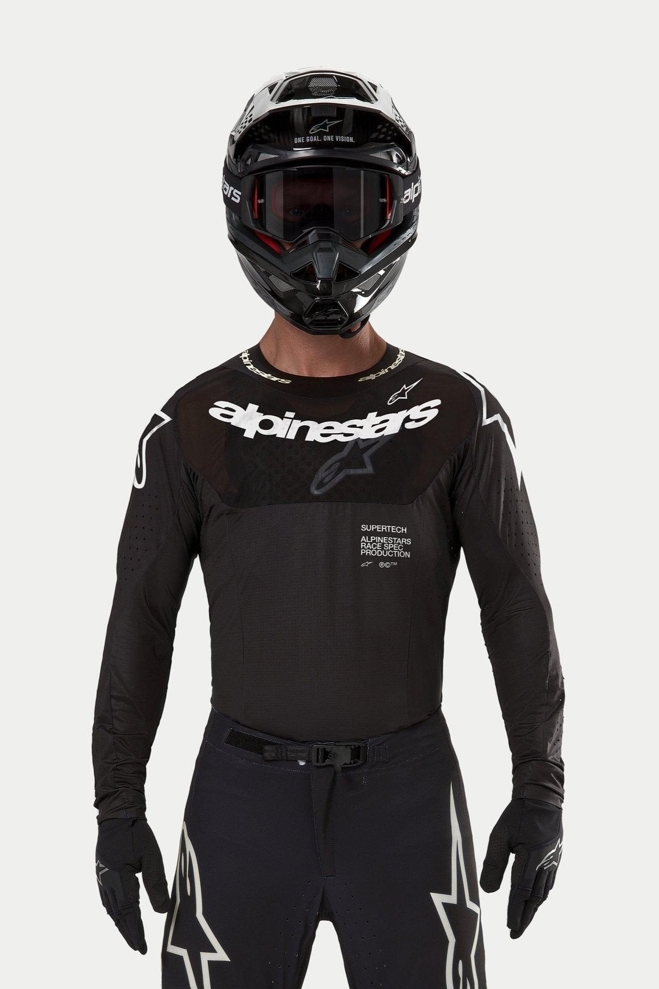 Motorcrossrijder die de Alpinestars 2024 Supertech Ward Jersey in het zwart draagt, atletische racepasvorm met wit Alpinestars-logo op de borst, voorzien van lasergesneden perforaties en de tekst 'Supertech Race Spec', gecombineerd met een zwarte helm en bril voor off-road racing.