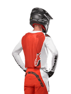 Alpinestars 2024 Supertech Ward Jersey, motorcross shirt in White Hot Orange, achteraanzicht met oranje rugpand en witte mouwen met zwart Alpinestars-logo, gecombineerd met bijpassende broek en een zwarte helm, professionele off-road race-uitrusting