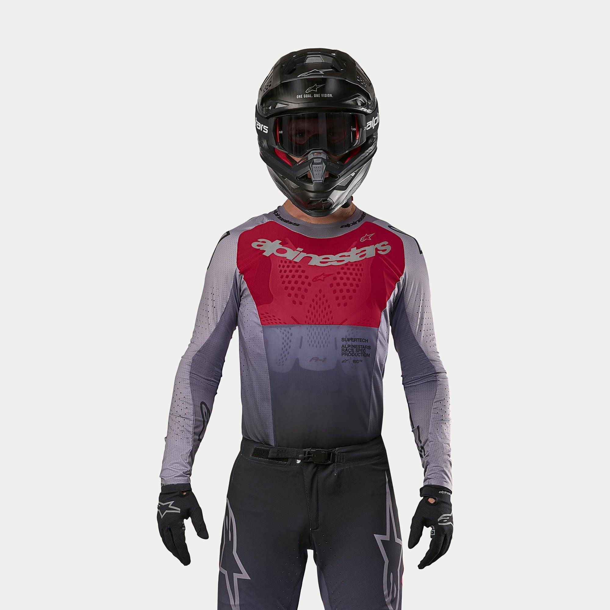 Alpinestars 2024 Supertech Dade Jersey in Iron Red Berry, motocross jersey met een rood borstpaneel en grijze mouwen met zilveren logo's, gedragen door een motocrosser met een bijpassende broek, zwarte helm en zwarte handschoenen, professionele off-road race-uitrusting