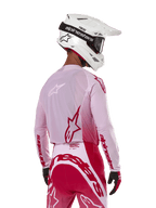 Alpinestars 2024 Supertech Dade Jersey in Red Berry Lilac, motorcrosser van achteren gezien, ademende mesh-panelen en rode Alpinestars-logo's, gecombineerd met een bijpassende rode en lila broek en een witte Alpinestars-helm met crossbril, professionele off-road race-uitrusting.