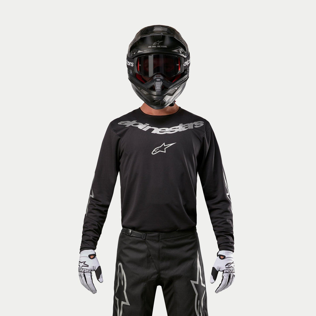 Alpinestars 2024 Fluid Graphite Jersey, zwart en zilveren motorcross jersey, gedragen door een rijder met een zwarte helm en rode bril, voorzien van zilveren Alpinestars branding op de borst, gecombineerd met een zwarte broek en witte handschoenen voor off-road prestaties