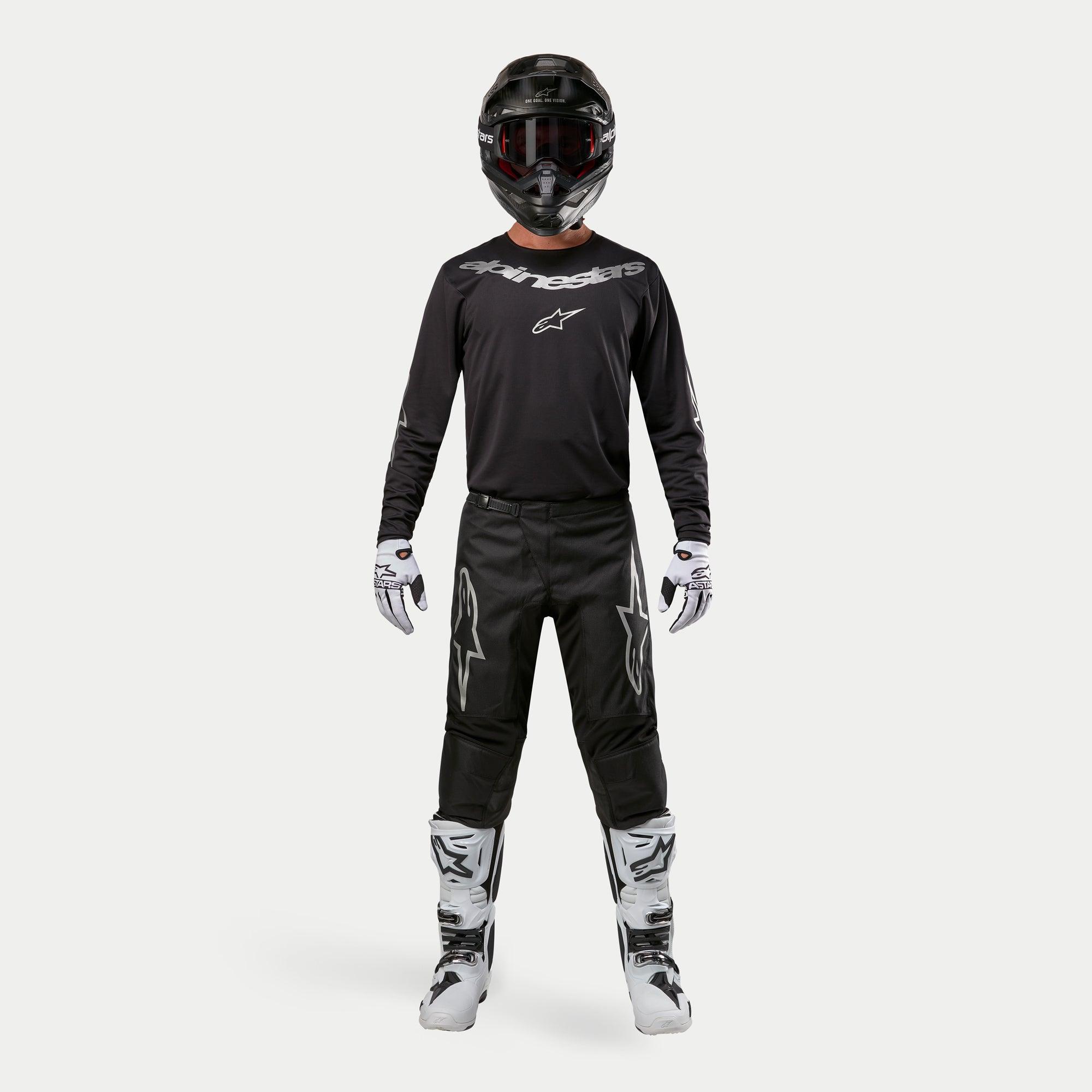 Motorcrossrijder in complete race-uitrusting, Alpinestars 2024 Fluid Graphite Jersey in Black Silver, zwarte broek met zilveren sterlogo's, zwarte helm met rode crossbril, wit-zwarte laarzen en handschoenen, gecoördineerde motorcross outfit