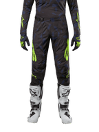 Alpinestars 2024 Techstar Rantera crossbroek, motorcross broek, zwart, navy en fluogeel, gedragen met bijpassende jersey met lange mouwen, handschoenen en witte motorcrosslaarzen, met opvallende neongele accenten en een abstract donker patroon.