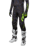 Alpinestars 2024 Techstar Rantera crossbroek, motorcrossbroek, zwart, navy en fluogeel, met navy camouflagepatronen en fluogroene logo's, gedragen met bijpassende handschoenen en witte laarzen, duurzaam racing-fit ontwerp voor off-road prestaties.