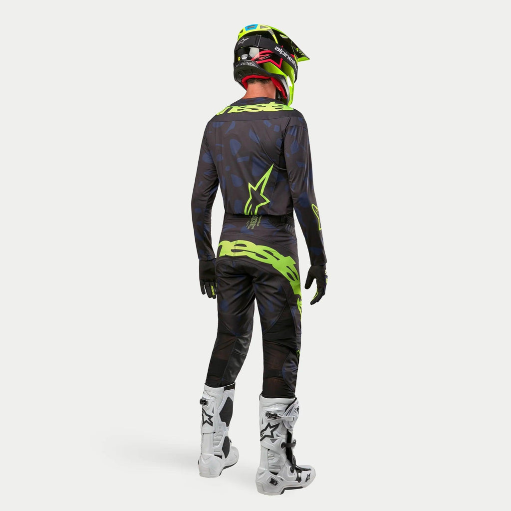 Alpinestars 2024 Techstar Rantera Jersey, motorcross shirt, zwart, navy en fluogeel, gedragen met bijpassende broek, witte en zwarte laarzen en een fluogele helm, van achteren gezien in complete off-road race-uitrusting
