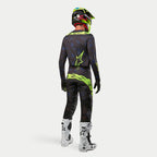 Alpinestars 2024 Techstar Rantera Jersey, motorcross shirt, zwart, navy en fluogeel, gedragen met bijpassende broek, witte en zwarte laarzen en een fluogele helm, van achteren gezien in complete off-road race-uitrusting