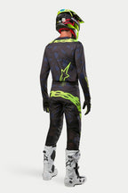 Alpinestars 2024 Techstar Rantera jersey en broek, motorcrosser in volledige uitrusting van achteren gezien, zwart, navy en fluogeel, bijpassende fluogele helm en witte laarzen, gecoördineerde off-road racekit