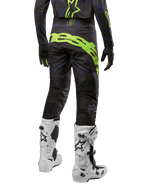 Alpinestars 2024 Techstar Rantera broek, motorcross broek, zwart, navy blauw en fluo geel, achteraanzicht, met opvallende neongele branding en mesh ventilatiepanelen, gedragen met bijpassende jersey en witte laarzen, duurzame uitrusting voor motorcross en off-road racing