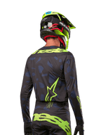 Achteraanzicht van een motorcrossrijder die het Alpinestars 2024 Techstar Rantera Jersey draagt in Black Navy Yellow Fluo, met opvallende fluo-gele branding en logo's op de rug, gecombineerd met een bijpassende motorcrossbroek en een neongele helm voor een complete off-road racing-look.