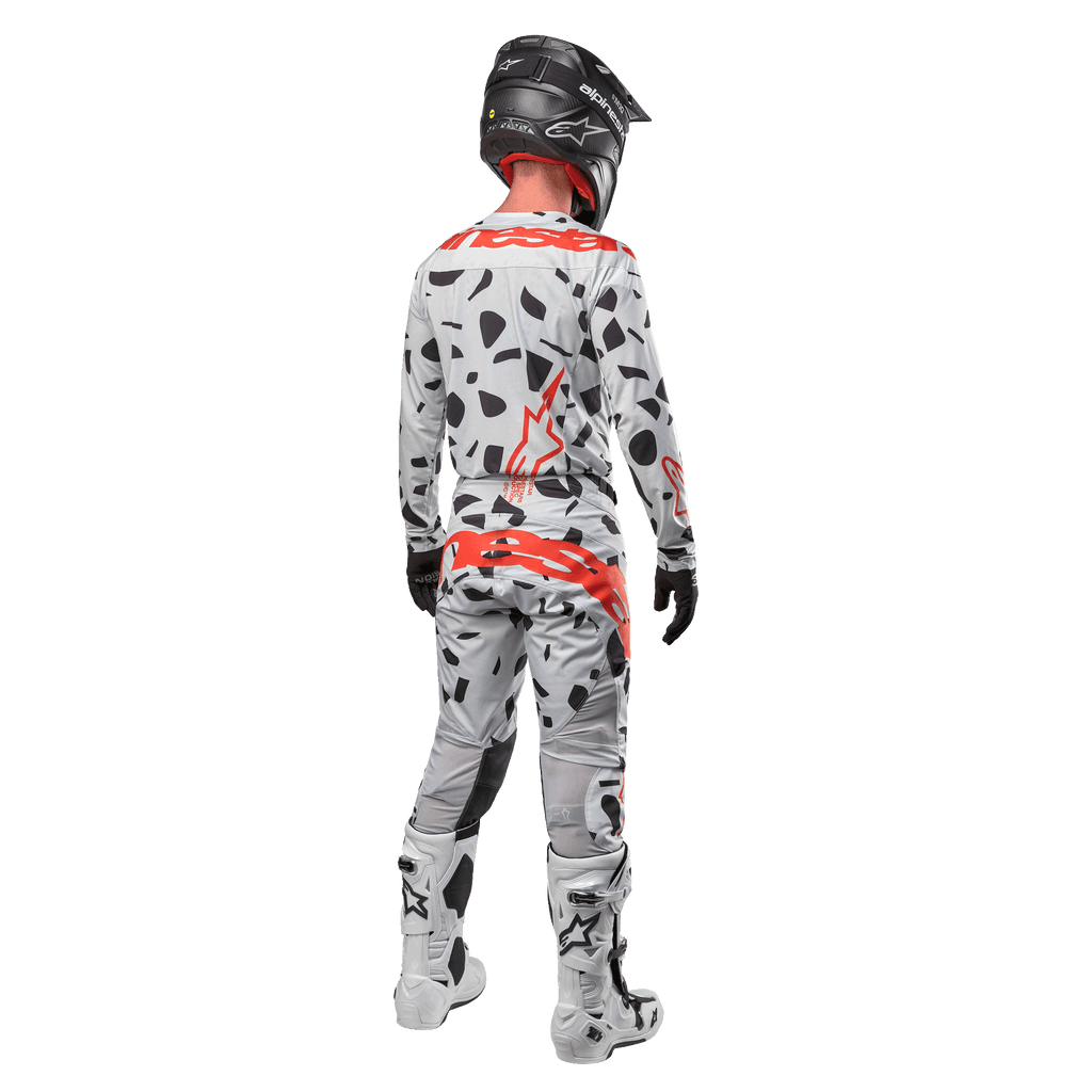 Motocrosser van achteren in Alpinestars 2024 Techstar Rantera Jersey en bijpassende broek, Haze Gray Camo-patroon met opvallende rode Alpinestars-logo's, zwarte helm, witte en zwarte laarzen, zwarte handschoenen, gecoördineerde motorcross-set.