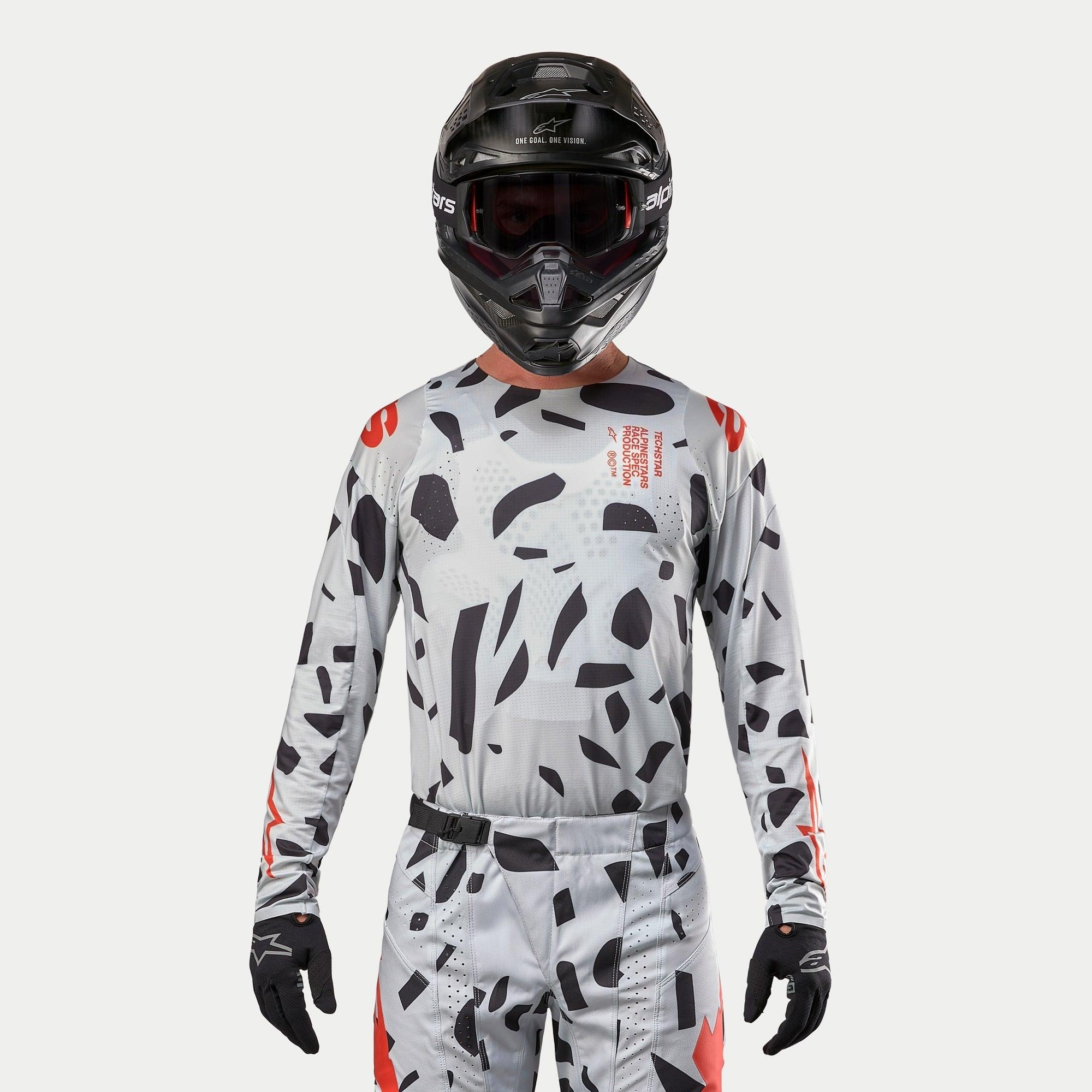 Alpinestars 2024 Techstar Rantera Jersey, motorcross jersey, Haze Gray Camo met zwarte onregelmatige patronen en rode accenten, gedragen door een rijder met bijpassende broek, zwarte helm en handschoenen, off-road race-uitrusting.