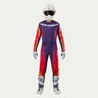 Alpinestars 2024 Techstar Pneuma motorcross outfit, compleet tenue met jersey en broek, donkerpaars met oranje en diepblauw, wit logo op de borst, inclusief witte helm en laarzen, persoon in volledige motorcross uitrusting